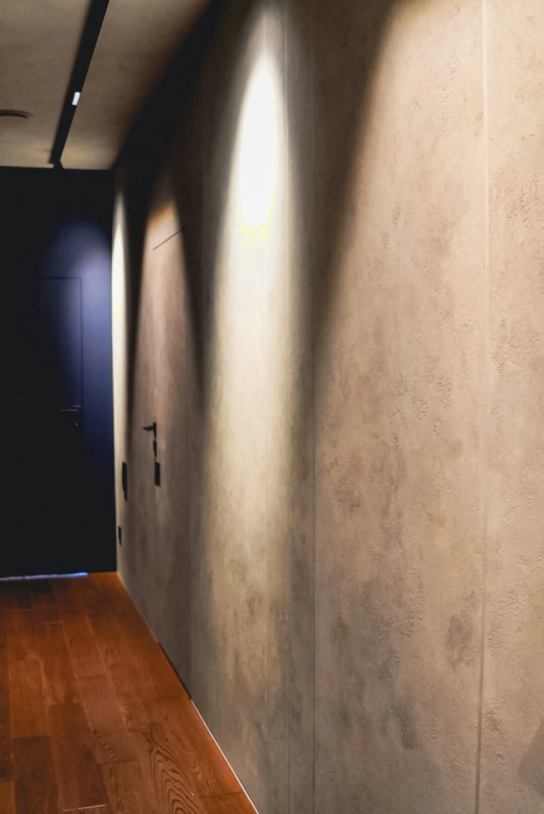 Tynki strukturalne: korytarz z szarym, teksturowanym tynkiem, drewnianą podłogą i sufitowym oświetleniem