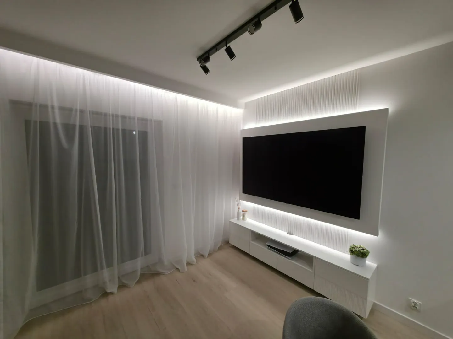 Nowoczesny salon z podświetlanym sufitem podwieszanym, ściennym telewizorem i zabudową RTV Sufity podwieszane