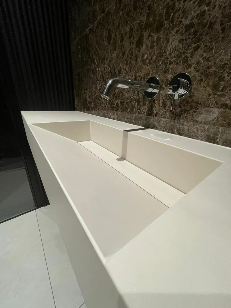 Biała umywalka z konglomeratu z chromowaną armaturą na tle marmurowej ściany Umywalki