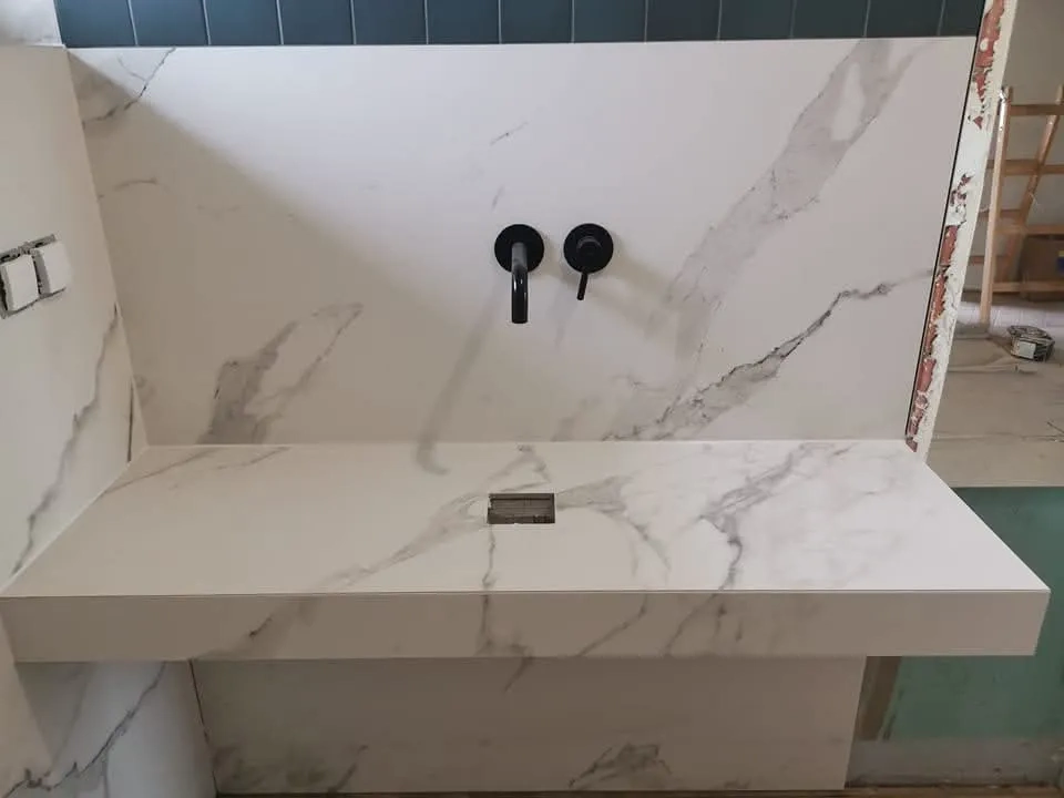 Umywalki: kwarcowa umywalka ścienna z białym marmurkowym blatem i czarną baterią na etapie montażu