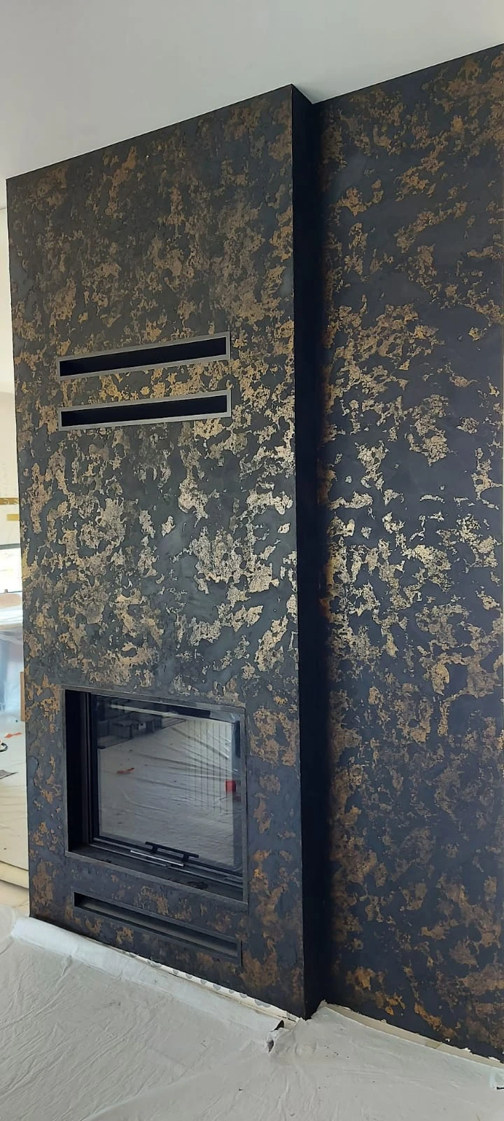 Nowoczesna zabudowa kominkowa wykończona płytami węglowymi z metalicznym złotym dekorem