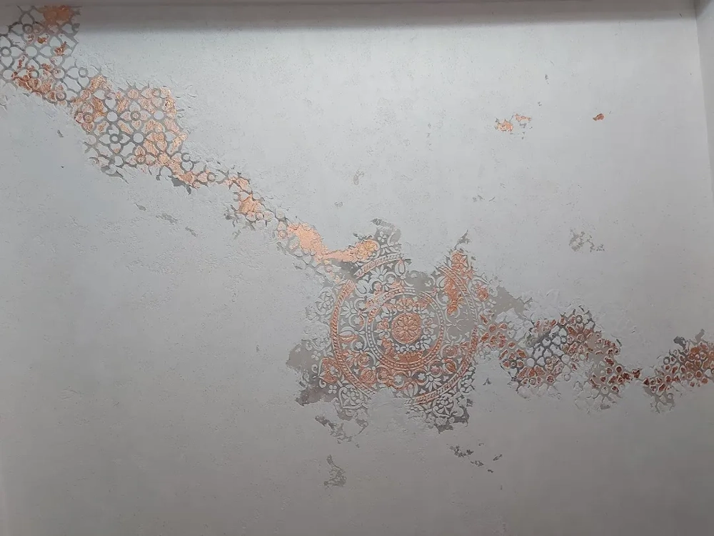Tynkowanie: dekoracyjny tynk ścienny z metalicznym wzorem mandali i fragmentami odsłoniętej warstwy