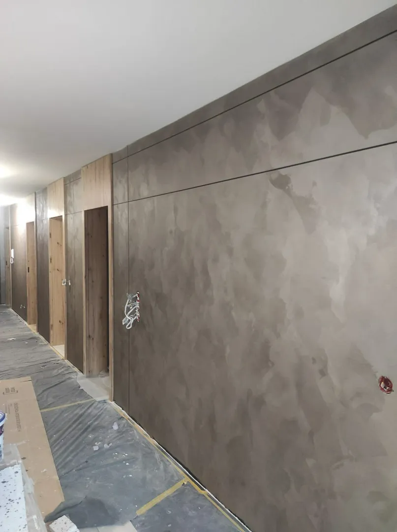 Korytarz ze świeżo wygładzonymi ścianami, otworami drzwiowymi i folią ochronną na podłodze, Tynkowanie