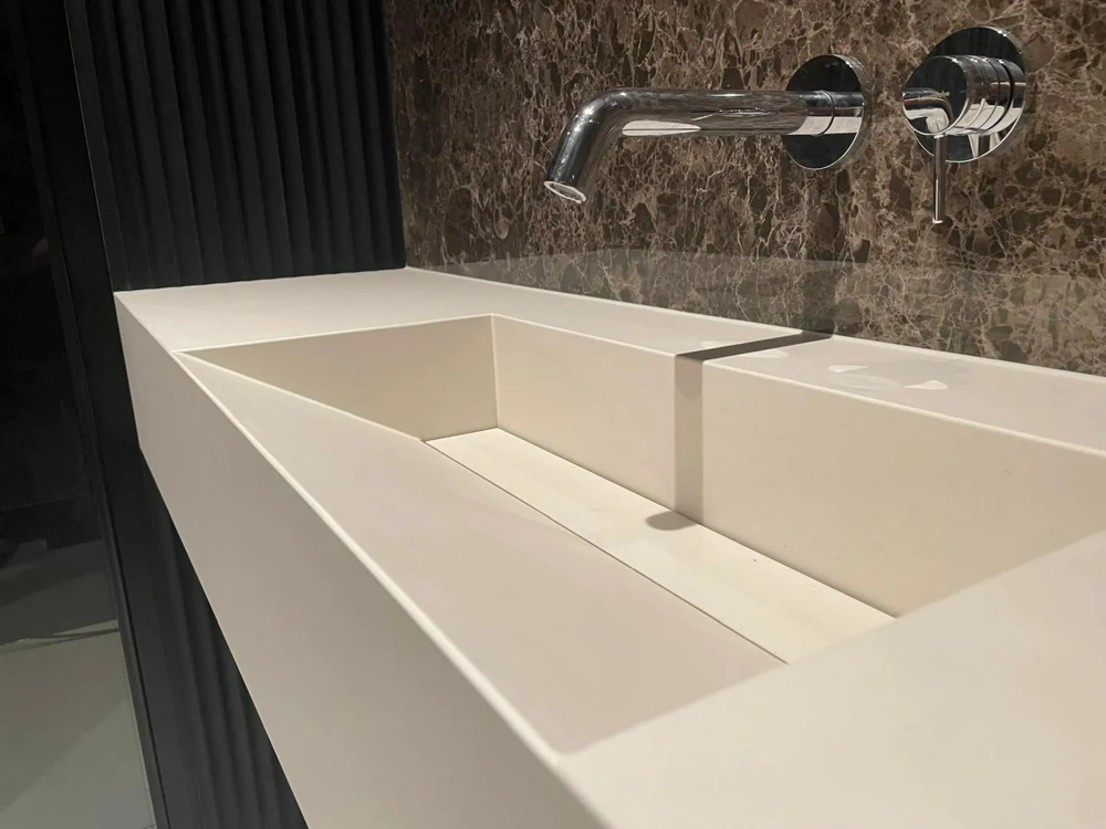 Umywalki z konglomeratu kwarcowego: biała minimalistyczna umywalka z podtynkową chromowaną baterią i marmurowym panelem