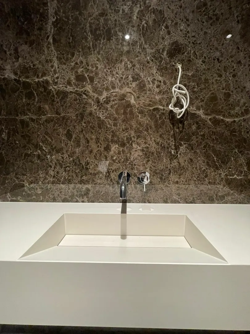 Umywalki nowoczesna biała umywalka wpuszczana w blat z baterią ścienną na tle marmurowej ściany