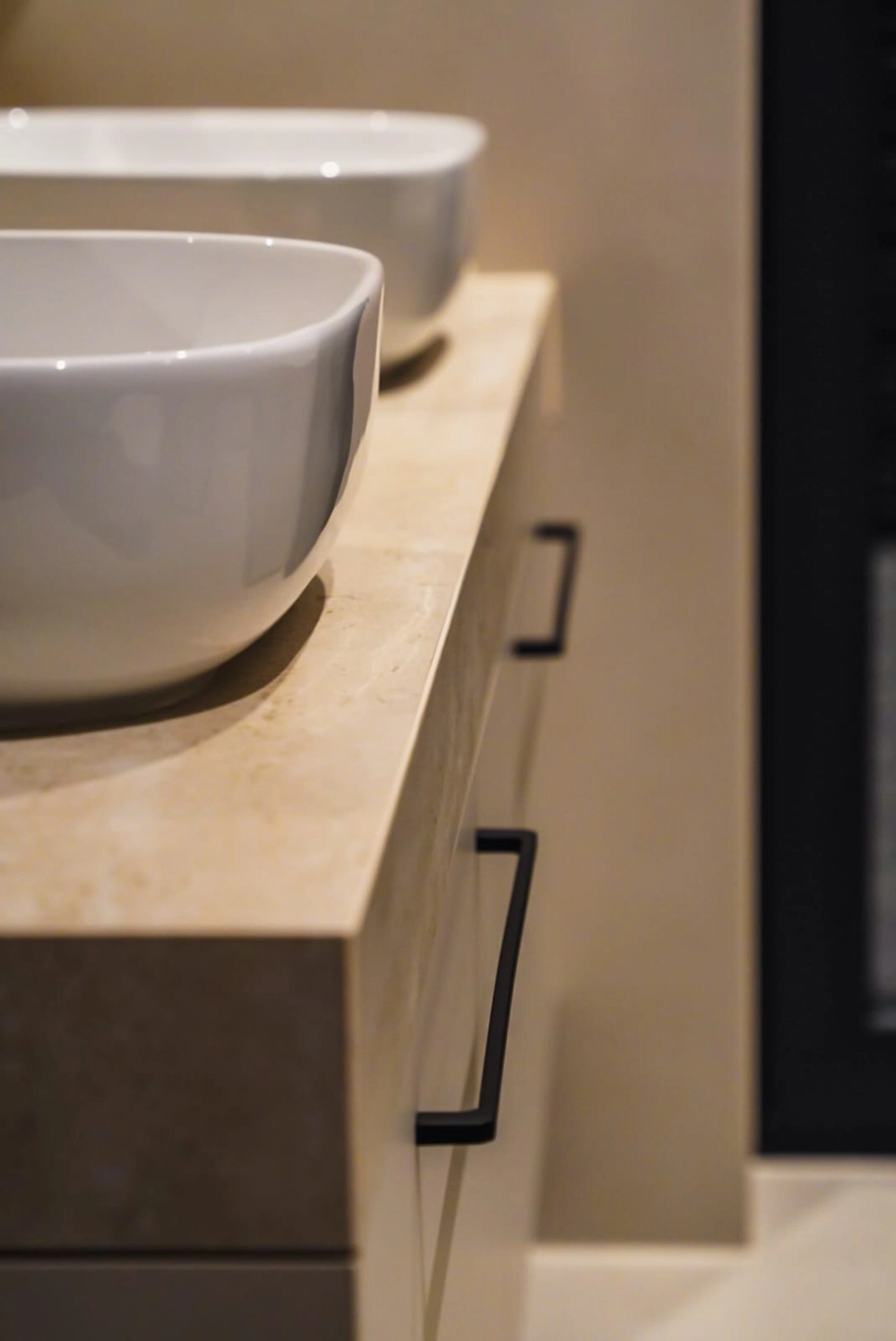 Nowoczesne okrągłe umywalki nablatowe na kamiennym blacie z czarnymi uchwytami frontów