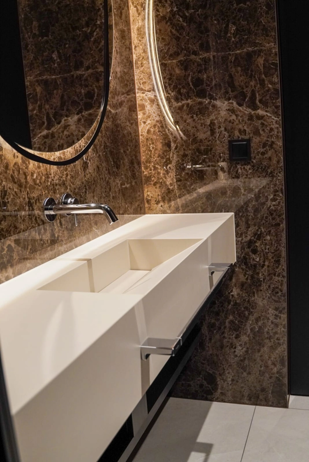 biała kwarcowa umywalka wpuszczana w blat na tle marmurowej ściany z podświetlanym lustrem Umywalki