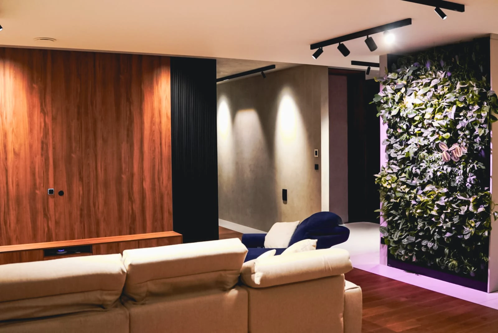 Nowoczesny salon z drewnianą ścianą TV, podwieszanym oświetleniem i zielonym panelem roślinnym – aranżacja wnętrz