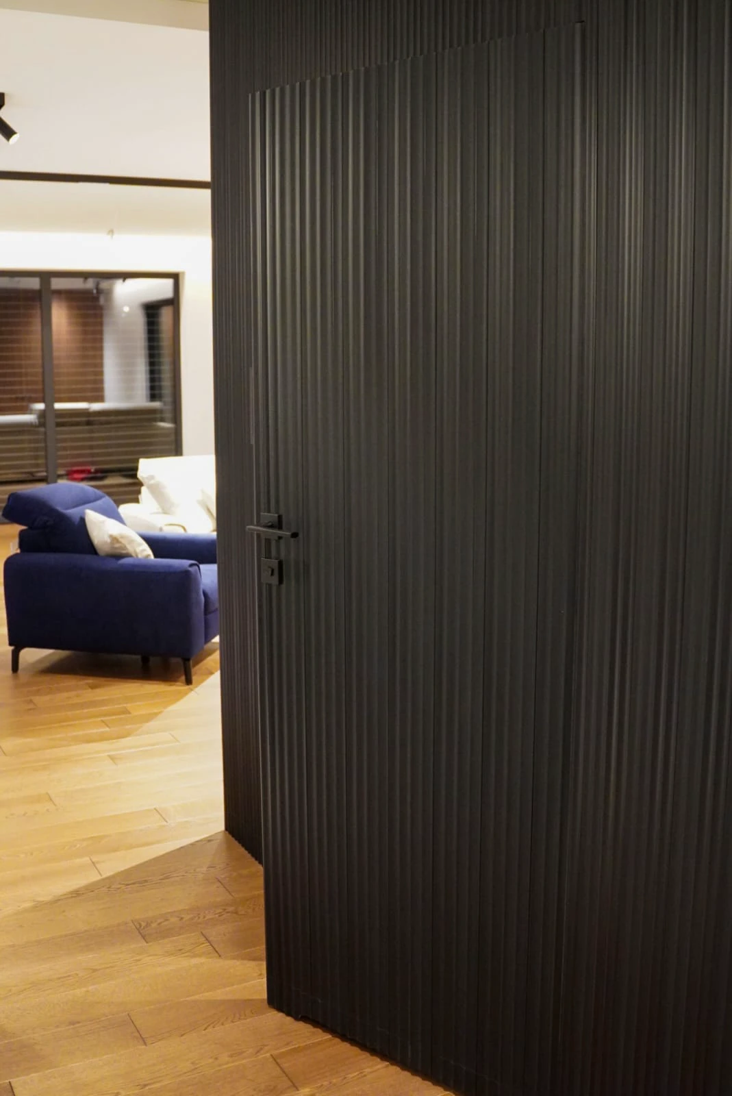 Montaż drzwi: czarne ryflowane drzwi wewnętrzne otwarte na salon z drewnianą podłogą i granatową sofą