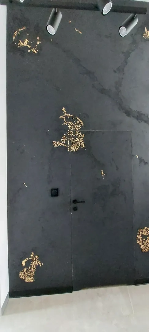 Czarna ściana z ukrytą drzwiami wykończona złotymi ornamentami, sztukateria