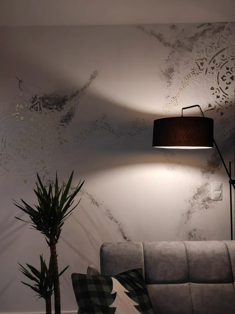 Nowoczesna aranżacja wnętrz z dekoracyjnym tynkowaniem, lampą stojącą, szarą sofą i rośliną doniczkową