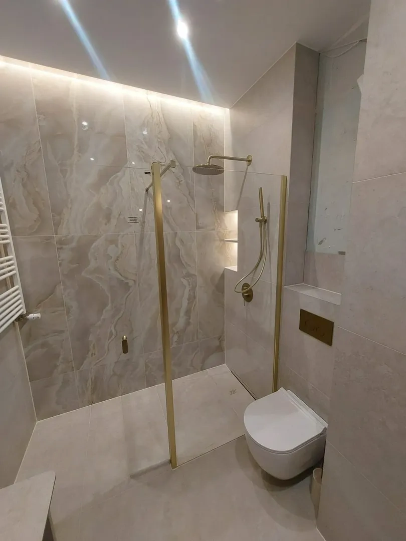 Remont łazienki: nowoczesna łazienka z wielkoformatowymi płytkami, szklaną kabiną i złotą armaturą