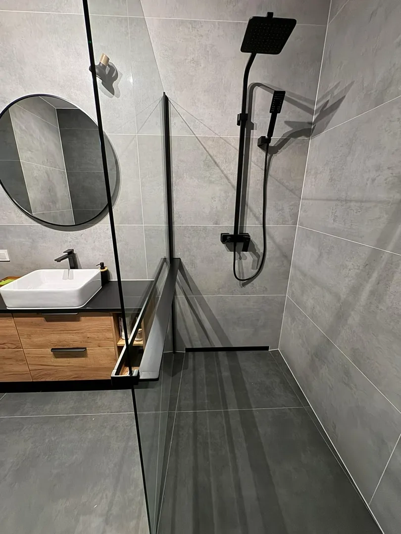 Remont łazienki: nowoczesna łazienka z szarymi płytkami wielkoformatowymi, czarną armaturą, szklaną ścianką prysznicową i szafką pod umywalkę