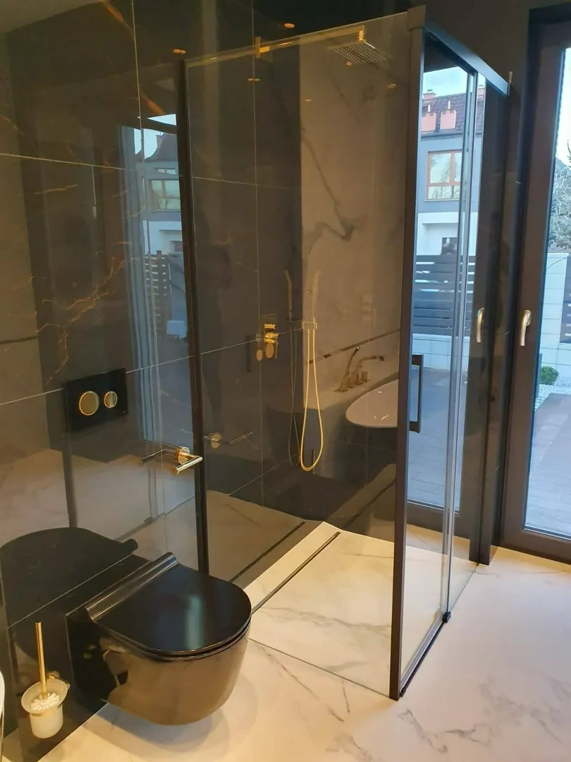 Nowoczesna łazienka z czarną toaletą i szklaną kabiną prysznicową na marmurowych płytkach – Remont łazienki