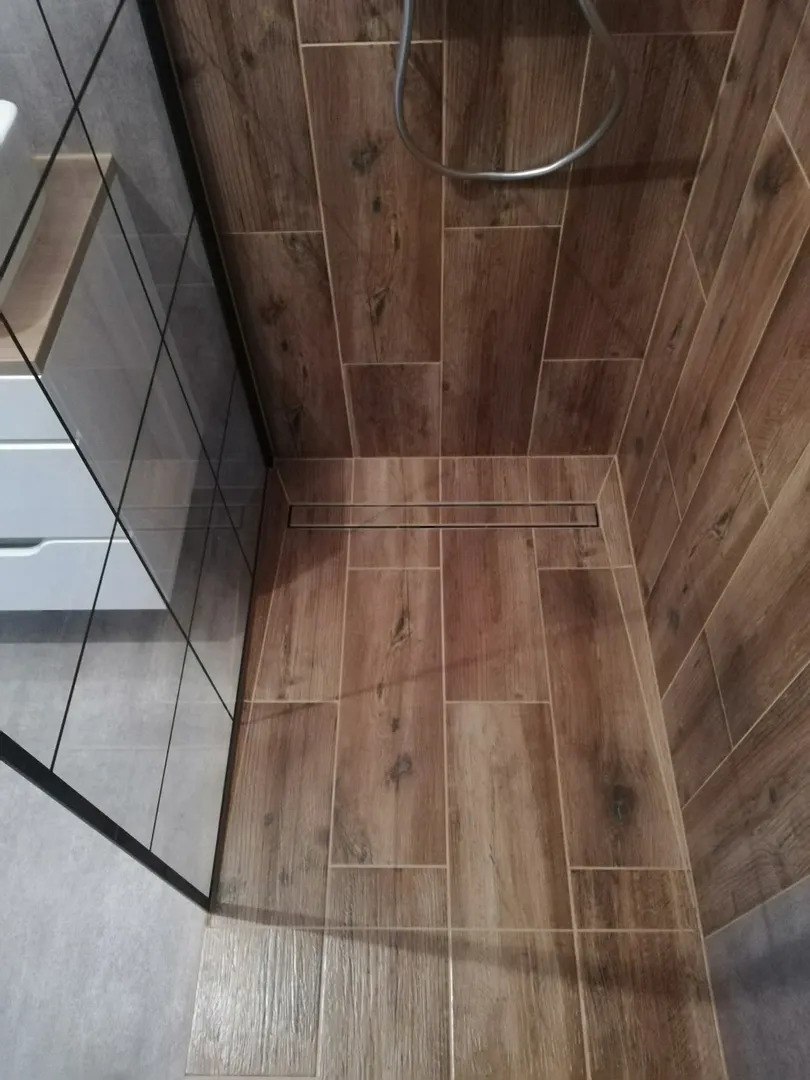 Strefa prysznica wykończona drewnopodobnymi płytkami z liniowym odpływem – układanie płytek